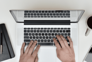 Computer on a white table with an individual typing on the keyboard