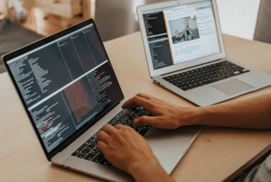 A man coding on a laptop sat at a wooden table