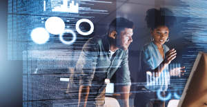 A man and a woman are stood looking at a grey computer. There is an effect to show code in the background of the image